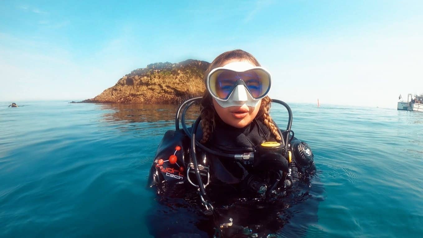 diver in water at surface with rock and boat in background