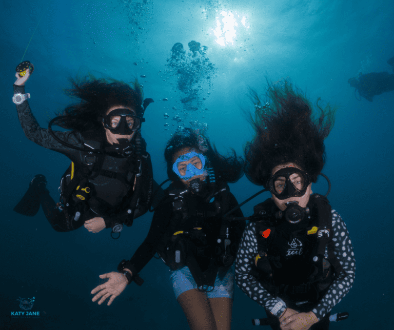 three scuba divers underwater with hair messy