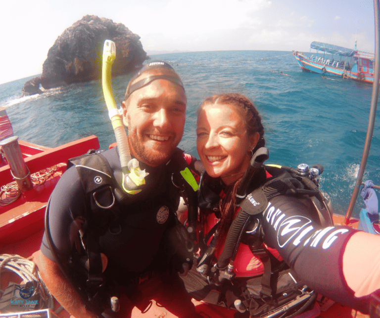 two divers on boat in front of rock pinnacle and ocean