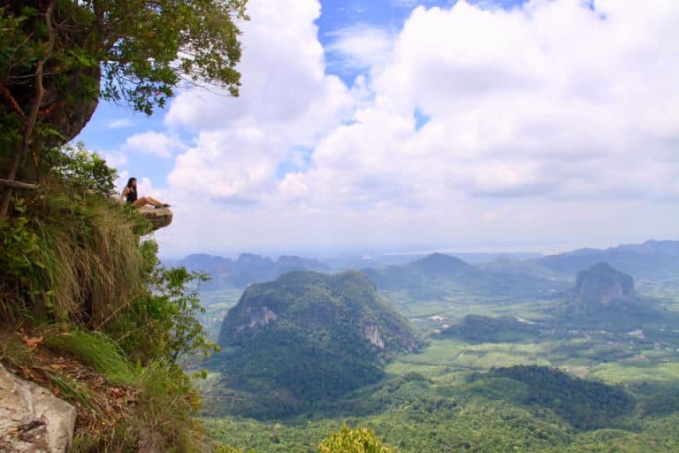 person sitting on high cliff with views of jungles and mountains