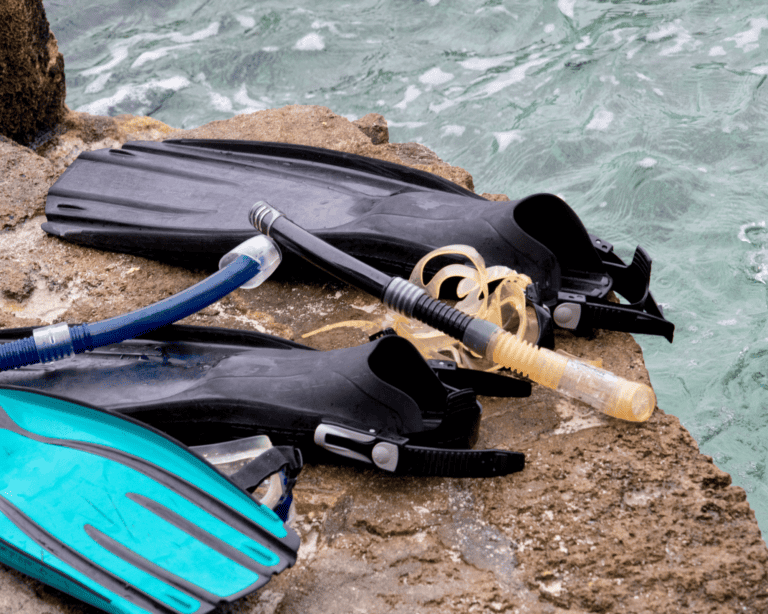 two sets of snorkel and fins on a rock next to water