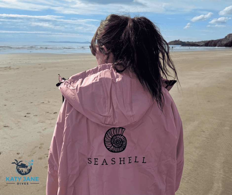 person from behind standing on a beach with dark hair in pink changing robe with seashell design