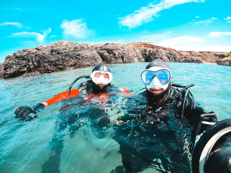 Two scuba divers in clear blue water with blue skies