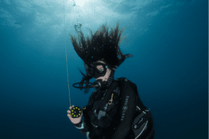 Katy Jane scuba diving underwater with an SMB with a blue ocean background and wavy hair