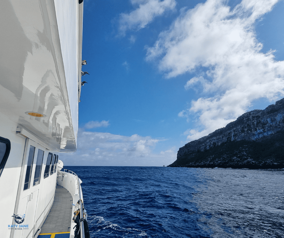 photo of side of boat with ocean and big rocky island