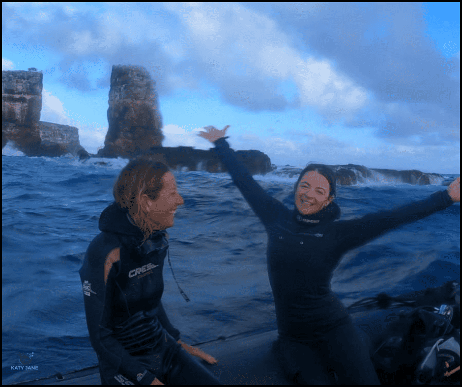 two divers in wetsuit on small boat in front of darwins pillars