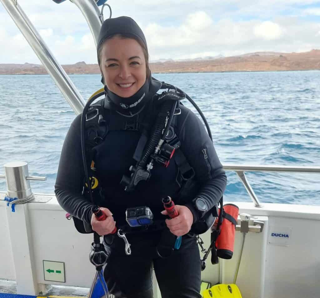 katy jane dives in scuba gear on a boat with ocean and island in background
