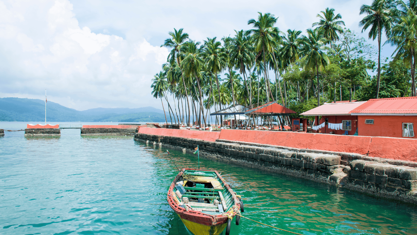 image of boat with clear blue green water and small buildings and trees